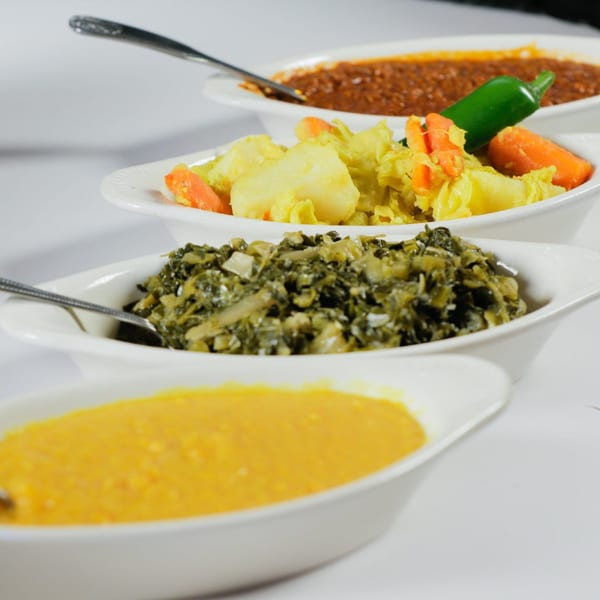 Four white oval bowls filled with various Ethiopian dishes, including stews and vegetables.
