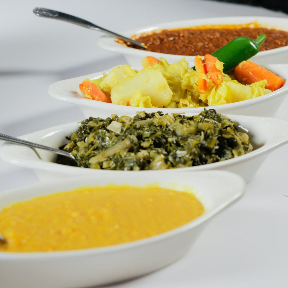 Four white oval bowls filled with various Ethiopian dishes, including stews and vegetables.