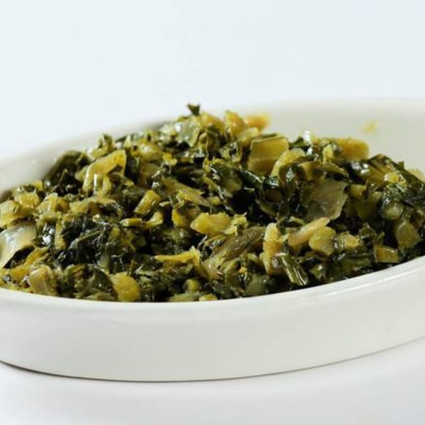 A white oval dish filled with Messob Ethiopian Restaurant's green and yellow Gomen, a collard greens dish.
