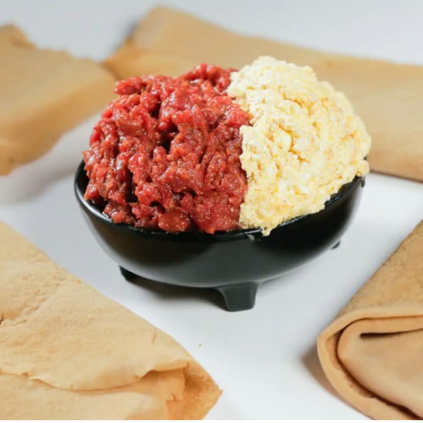 A black bowl filled with red kitfo and yellow ayib, surrounded by injera bread.