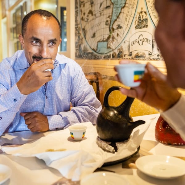 Two men enjoying Ethiopian coffee, with a traditional jebena and cups on the table.