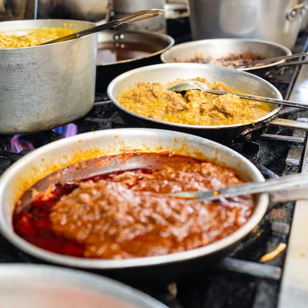 Pots and pans of Ethiopian stews, including a red stew and a yellow stew, cooking on a stove.