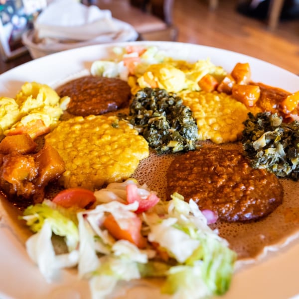 A large platter of Ethiopian food with various colorful stews, vegetables, and injera bread.