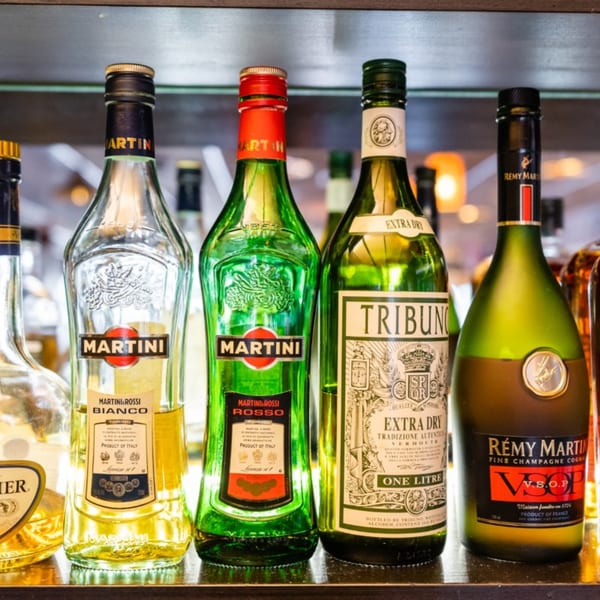 A close-up of various liquor bottles, including Martini and Rémy Martin, on a bar shelf.