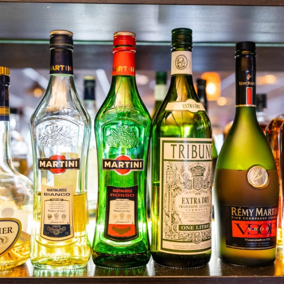 A close-up of various liquor bottles, including Martini and Rémy Martin, on a bar shelf.