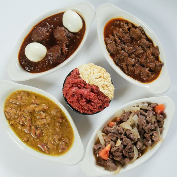Four oval dishes of Ethiopian stews and a central bowl of red and white minced meat.