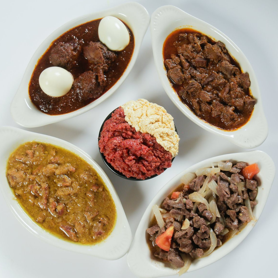Four oval dishes of Ethiopian stews and a central bowl of red and white minced meat.