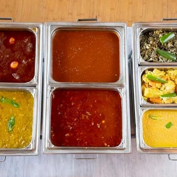 Six metal trays filled with various Ethiopian stews and dishes, including red, yellow, and green options.