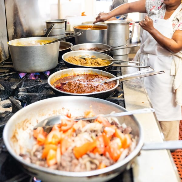A chef prepares various Ethiopian dishes in large pots and pans on a commercial stove.