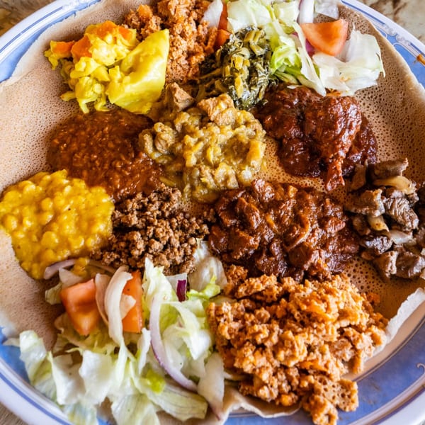 A large platter of Messob Ethiopian food with various colorful stews, meats, and vegetables on injera.