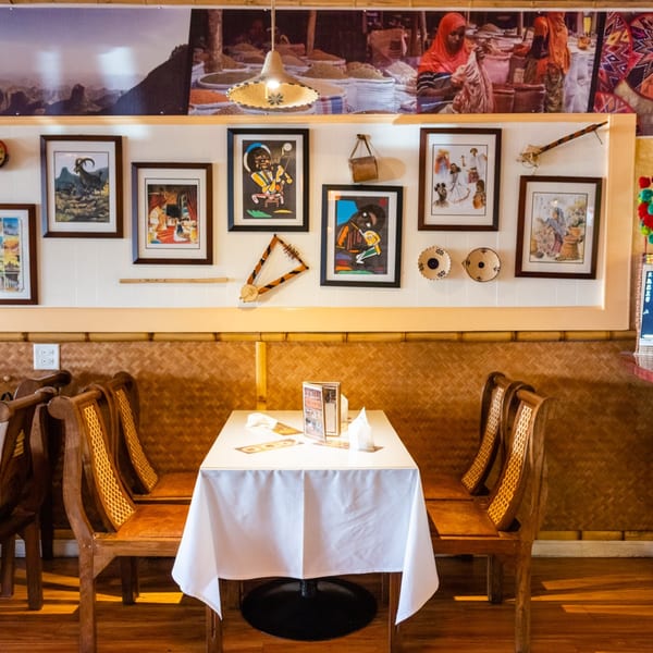 Messob Ethiopian Restaurant interior with a table, chairs, and Ethiopian art on the wall.