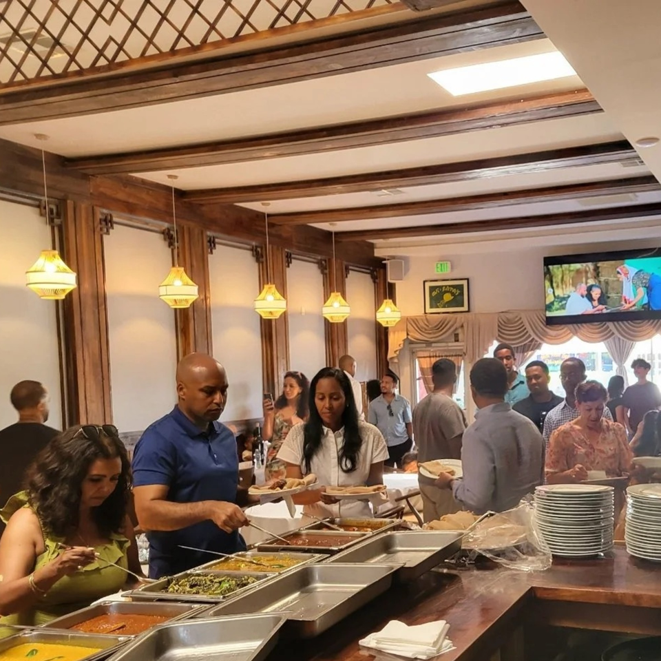 Customers at Messob Ethiopian Restaurant serving themselves from a buffet line with various dishes.