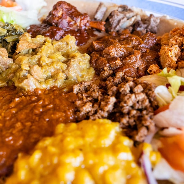 Close-up of a vibrant Messob Ethiopian Restaurant platter with various stews, meats, and vegetables.