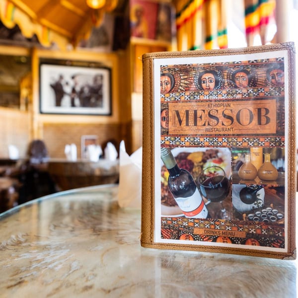 Messob Ethiopian Restaurant menu on a marble table, with a blurred restaurant interior in the background.