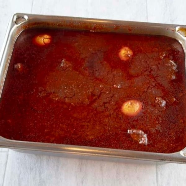 A large metal pan filled with a rich, dark red Ethiopian stew, featuring several whole eggs.